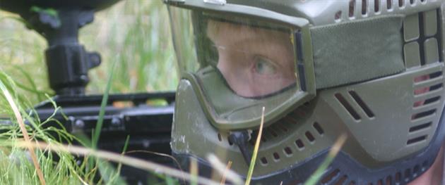 Paintballspelare i ansiktsmask i gräset, Paintballtorpet