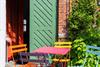 Green door with orange curtain and colourful café chairs at Sentralbadet's entrance in Odda, framed by green leaves.
