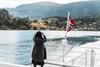 Passasjer fotograferer fjordlandskapet frå akterdekket under fjordcruise på Hardangerfjorden, norsk flagg i vinden.