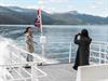 To passasjerar tar selfie på akterdekket under fjordcruise på Hardangerfjorden, snødekte fjell i bakgrunnen.