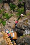 Deltakar i rosa jakke tek første steg opp bergveggen ved via ferrata-starten på Valhall i Odda, medan gruppa ventar på plattformen nedanfor.