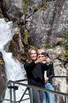To unge kvinner tar selfie framfor ein foss i Hardanger under eit fjordcruise-stopp.