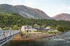 A large wooden white guesthouse next to a river and a walking bridge.