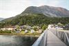 En liten campingplass ved en elv, omgitt av grøntområder og høye fjell.