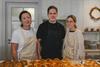 A few of the bakery staff posing behind a table of baked goods.