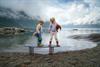 Zwei Kinder stehen auf einem Spiel-Surfbrett mit dem Fjord im Hintergrund.