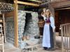 i kvinne i Hardangerbunad har omvising i ein av stovene på Hardanger folkemuseum. Ho står foran et ildsted av stein inne i en gammel lafta stove, det er dekor på treveggene og gamle gjenstander står på gulvet og henger på veggen
