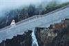 Eine Frau in einem weißen Pullover steht auf der Brücke über dem Vøringsfossen.