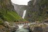 Menschen in roter Kleidung, die norwegische Flaggen schwenken, stehen auf der neuen Brücke; im Hintergrund ist der Wasserfall zu sehen.
