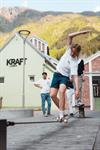 A young person performs a skateboard trick in the square outside KraftLaben in Odda, with the green mountains of Hardanger as a backdrop.