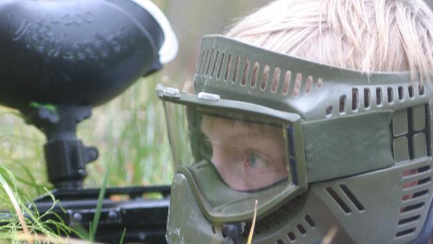Paintballspelare i ansiktsmask i gräset, Paintballtorpet