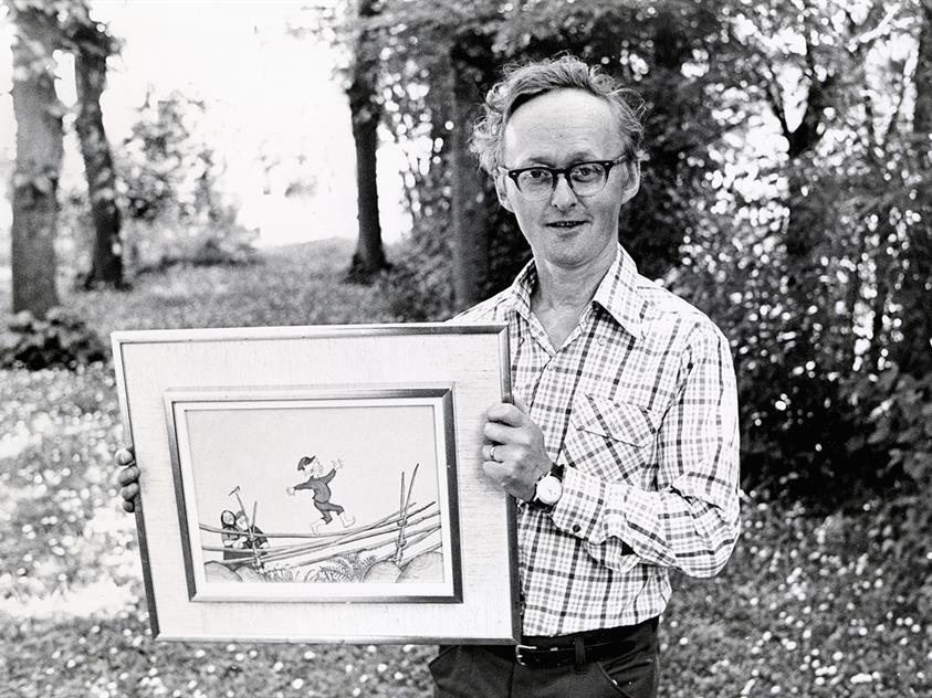 Ett svartvitt foto av konstnären Björn Berg som håller i en inramad originalteckning till Emil i Lönneberga., © Foto: Pehr Hasselroth